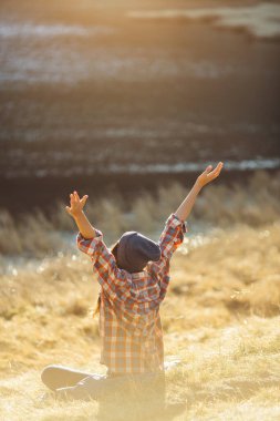 A woman in a plaid shirt and hat raises her arms in celebration while sitting near Nesamovyte Lake in the Carpathian Mountains, Ukraine. This high-quality image captures the joy of nature and outdoor clipart