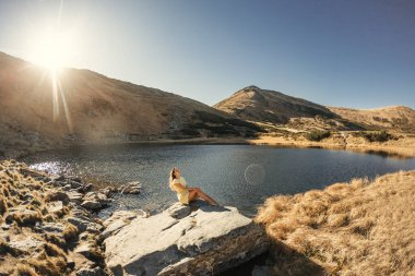 A woman basks in the sunlight by Nesamovyte Lake in the Carpathian Mountains, Ukraine. The tranquil environment and stunning natural beauty make this high-quality photo perfect for travel clipart