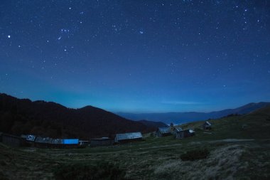 Huzurlu bir yıldızlı gece gökyüzü Ukrayna 'nın Karpat Dağları' nda yuva yapmış kırsal bir köyü aydınlatıyor. Bu yüksek kaliteli görüntü doğanın sükunetini ve güzelliğini yansıtıyor. Seyahat kavramları için ideal.