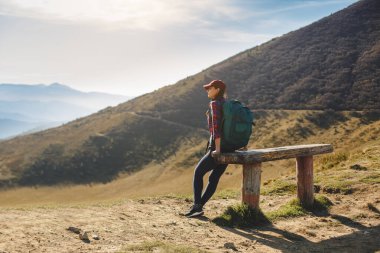 Sırt çantalı bir kadın yürüyüşçü, Karpat Dağları 'nın nefes kesici manzarasının tadını çıkarırken bir bankta mola veriyor. Seyahat, macera ve doğa kavramları için mükemmel bir görüntü.