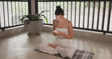 Salonda rahat bir yerde lotus pozisyonunda oturan bir kadın akıllı telefonunu kullanır. Farkındalık uygulamaları, yoga, sağlık veya meditasyon ve fitness uygulamalarına teknolojik entegrasyon içeren konular için mükemmel..