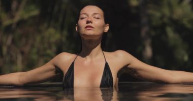 Tropik cennet, bikini plaj modelinin sonsuz havuzdaki siyah mayolu lüks rahatlığı. Yüzme havuzunda genç bir kadını yüzdürmek ve yıkamak.