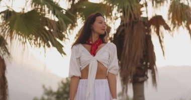 Beyaz elbiseli ve kırmızı eşarplı şık bir kadının tropikal ortamın tadını çıkarırken çekilmiş yavaş çekim görüntüleri. Seyahat blogları, moda promosyonları ve yaşam tarzı içeriği için mükemmel.