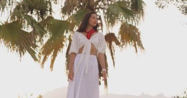 Beyaz elbiseli, kırmızı eşarplı, tropikal tatilin tadını çıkaran şık bir kadının yüksek kalite görüntüsü. Seyahat blogları, moda promosyonları ve yaşam tarzı içeriği için mükemmel.