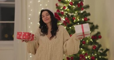 Parlak ışıkları olan güzel dekore edilmiş bir ağacın önünde kırmızı ve beyaz Noel hediyeleriyle dans eden hoş bir kadın. Bayram promosyonları ve mevsimlik selamlar için ideal..