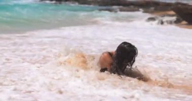 Bikinili bir kadının sahilde ona çarpan bir okyanus dalgası tarafından şaşırtıldığı eğlenceli yavaş çekim görüntüleri. Seyahat promosyonları, plaj temalı reklamlar ve yaşam tarzı içeriği için mükemmel.. 