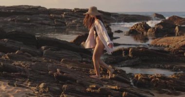 Siyah kesim mayo, güneş şapkası ve Sri Lanka 'da gün doğumunda kayalık bir plajı keşfeden bir kadın. Seyahat reklamları, tropikal tatil promosyonları ve huzur veren yaşam tarzı içeriği için mükemmel.