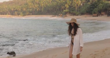 Sri Lanka 'daki Silent Beach' te siyah mayolu ve güneş şapkalı bir kadının yavaş çekim görüntüleri. Seyahat promosyonları, tropikal tatil reklamları ve yaşam tarzı içeriği için ideal.