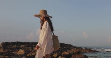 Güneş şapkalı ve plajlı bir kadın Sri Lanka 'da Silent Beach' teki kayalık sahili keşfediyor. Seyahat promosyonlarında, tropikal tatil reklamlarında ve huzurlu ve huzurlu bir yaşam tarzında kullanım için mükemmel.