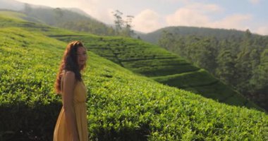 Sarı elbiseli bir kadın Nuwara Eliya, Sri Lanka 'daki yemyeşil çay tarlalarında yürüyor. Seyahat, doğa ve macera kavramları için idealdir. Promosyon ve editörlük için mükemmel. Yüksek kalite