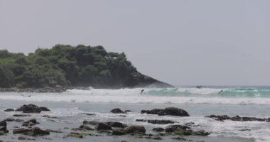 Sri Lanka 'daki Hiriketiya Sahili' nde sörfçüler, yemyeşil bir zemin ve kayalık bir kıyıya karşı atlayıp düşüyorlar. Yüksek kaliteli görsellerde macera, seyahat ve doğa kavramları için idealdir. 