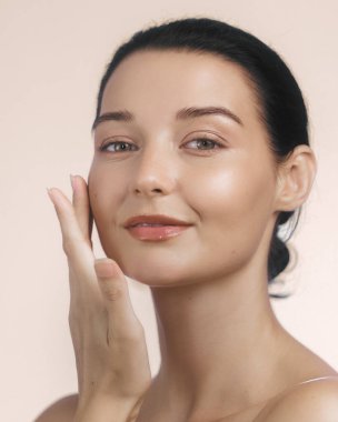 Yüzüne nazikçe dokunan, parlak tenli, doğal makyajlı, beyaz bir kadının yakın çekimi. Güzellik, cilt bakımı ve refah kavramları için idealdir. Yüksek çözünürlüklü resim promosyon kullanımı için mükemmel.