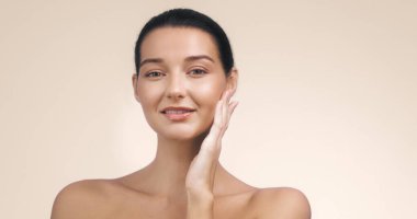 Işıl ışıl gülümseyen genç bir kadın yüzüne hafifçe dokunur, parıldayan cildini ön plana çıkarır. Minimalist arka plan doğal güzelliğini arttırarak bu görüntüyü cilt bakımı, güzellik ve...