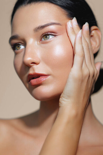 Красивый портрет латиноамериканки с сияющей кожей и натуральным макияжем, нежно ласкающей лицо обеими руками на теплом бежевом фоне. Перфект для скинхедов, красота