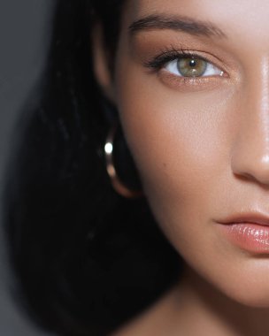 Bir kadının kusursuz derisini ve zarif halka küpesini gösteren, doğal güzelliği ön plana çıkaran minimalist yakın plan bir portre. Güzellik reklamları, cilt bakımı promosyonları ve moda kampanyaları için mükemmel.