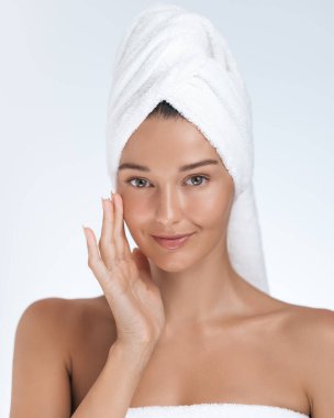 Işıl ışıl cildi olan genç bir kadın ferahlatıcı bir banyodan sonra havluya sarılıp yüzüne krem sürüyor. Güzellik, sağlık ve cilt bakım ürünleri reklamları veya promosyonlar için mükemmel..