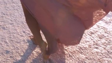 Güneş doğarken tuz gölünde yürüyen çıplak ayaklı bir kadının yakın çekimi, yumuşak ışığa yakalanan elbisesi. Huzurlu sahne, doğayla bir bağ ve sakinlik hissi uyandırır. Seyahat için idealdir.