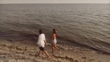 Kumsalda yürüyen bir çiftin hava görüntüsü, bir dron tarafından yakalandı. Seyahat promosyonları, romantik kaçamak reklamları ve tatil kampanyaları için ideal..