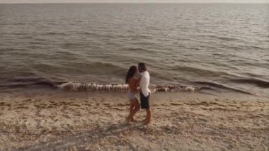 Bir adamın kumlu bir sahilde koşarken bir kadını kollarıyla kaldırışının sinematik yavaş çekim görüntüleri. Seyahat blogları, yaz promosyonları ve yaşam tarzı içeriği için mükemmel.