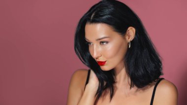 Kalın kırmızı dudakları ve pembe arka planda poz veren parlak siyah saçları olan şık bir kadın. Parlak cildi ve şık görünüşü bunu moda, güzellik ya da kozmetik ürünler için mükemmel kılıyor..