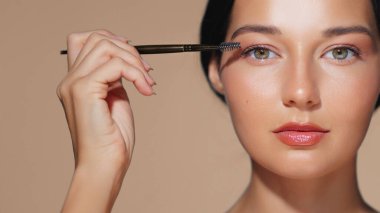 Kaşlarını bir fırçayla dikkatlice tımar eden kadın parıldayan derisini ve doğal güzelliğini sergiliyor. Güzellik ürünlerini, makyaj derslerini veya cilt rutinlerini geliştirmek için mükemmeldir.