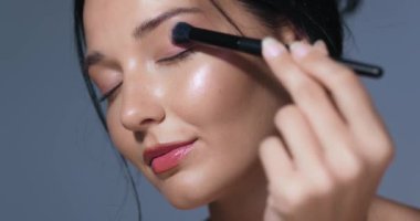 Asyalı bir kadının, parlak cildini gösteren bir fırçayla fosforlu kalem sürerken çekilmiş detaylı görüntüleri. Güzellik, cilt bakımı ve kozmetik reklamları için mükemmel. Yüksek kaliteli resim için uygun
