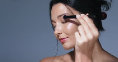 Bir kadının portresi fırçayla makyaj yapıyor, doğal güzelliğini ve parlayan cildini ön plana çıkarıyor. Güzellik, cilt bakımı ve makyaj reklamları ve yüksek kaliteli promosyon malzemeleri için ideal..