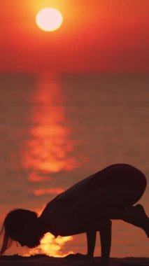 Gün doğumunda karga pozisyonunda dengede duran bir kadın, ışıldayan ufukta siluet oluşturur. Huzurlu sahne gücü, dengeyi ve farkındalığı yakalar. Fitness ve meditasyon için idealdir.