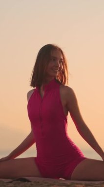 Bir kadın güneş doğarken kumsalda yoga pozu veriyor. Bu sakin yavaş çekim sahnesi esneklik ve gücün özünü yakalar. Form ve sağIık kavramları için mükemmeldir. Dikey