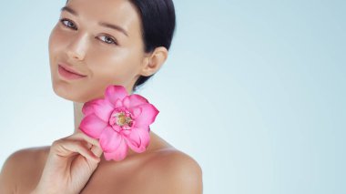 Elegant woman gently holding a pink lotus flower near her neck, symbolizing natural beauty and skincare. Ideal for wellness, spa treatments, beauty product advertisements, and luxury skincare clipart