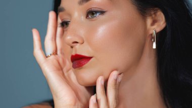 Close-up beauty portrait of an Asian woman with flawless skin, bold red lips, and elegant gold jewelry, posing gracefully with her hands. Ideal for cosmetics, skincare, and fashion promotions. clipart