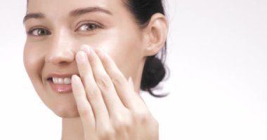 Işıl ışıl, nemli bir teni olan genç bir kadın yüzüne yumuşak bir gülümsemeyle krem sürüyor. Cilt bakımı ve doğal güzelliği destekleyen cilt bakımı ve sağlık kampanyaları için mükemmel..