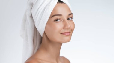 Cilt bakımını tamamladıktan sonra havluyla sarılıp sarılan ışıl ışıl cildi olan gülümseyen bir kadının yakın çekimi. Güzellik, cilt bakımı ve doğal güzelliğe odaklanan sağlık terfileri için mükemmel.