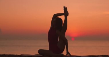 Gün doğumunda sahilde yoga yapan bir kadının silüeti. Bu barışçıl görüntü refahı, farkındalığı, plaj yogasını, sükuneti ve güzelliği arttırmak için idealdir.