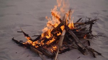 Kumlu bir sahilde yanan bir kamp ateşinin sinematik yavaş çekim görüntüleri. Açık hava macera blogları, kamp promosyonları ve doğa temalı içerik için mükemmel..