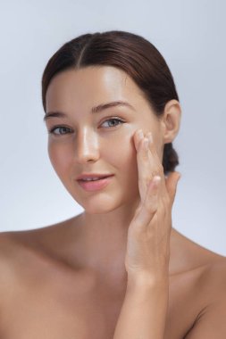 A young woman with glowing skin gently applies skincare to her face, showcasing her healthy, radiant complexion. Ideal for beauty, skincare, and self-care promotions, highlighting facial care and clipart