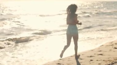 Enerjik bir kadın, turuncu bikinili ve kot şortlu, güneşli bir plaj boyunca koşuyor. Bu canlı sahne yaz eğlencesini, özgürlüğü ve kıyı maceralarını temsil ediyor..