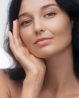 Yüzüne nazikçe dokunan kusursuz derisi olan, doğal güzelliği ve cildini ön plana çıkaran güzel bir genç kadının yakın çekimi. Güzellik, sağlık ve kozmetik reklamcılık için ideal..