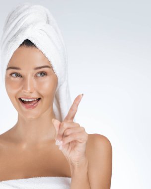 Kafasına havlu sarılmış şakacı bir kadın gülümser ve yukarı doğru işaret eder, heyecan ve neşe ifade eder. Güzelliği, kendine bakımı ve cilt bakımını desteklemek için idealdir.