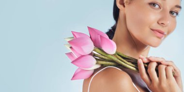 Omzunda pembe nilüfer çiçekleri tutan sakin Asyalı bir kadının profili güzellik, sağlık ve sükuneti temsil ediyor. Spa, cilt bakımı ve sağlık kavramlarını geliştirmek için mükemmel.