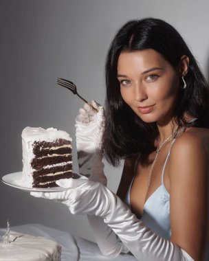 A glamorous woman in a blue dress and white gloves holds a plate with a slice of cake and a fork. This high-quality stock photo is perfect for promoting luxury, elegance, and special celebrations in clipart