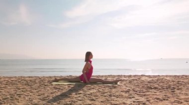 Güneş doğarken kumlu bir plajda yoga yapan bir kadın. Arka planda sakin bir okyanus var. Farkındalık, esneklik, açık hava fitness ve barışçıl doğa ayarları için idealdir..