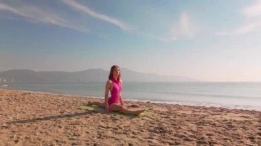 Bir kadın, sabah güneşinin altında, arkasında dağlar ve okyanuslar olan kumlu bir sahilde huzurlu bir yoga seansının tadını çıkarıyor. Refah, açık hava sporu ve farkındalık kavramları için mükemmel..