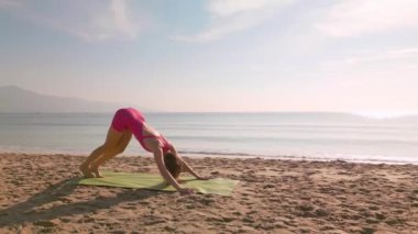 Bir kadın, Vietnam 'da, Da Nang' ın arka planında okyanus dalgaları ve dağlarla güneşli bir plajda yoga yapıyor. Sağlık, farkındalık, açık hava uygunluğu ve sakin yaşam tarzı görselleri için ideal..