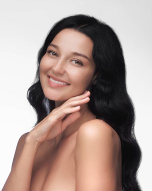 Temiz, parlak tenli ve koyu saçlı beyaz bir arka plana gülümseyen bir kadının neşeli bir portresi. Güzellik ve yaşam tarzı reklamcılığı için ideal..