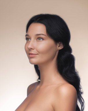 Uzun siyah saçlı, pürüzsüz ciltli, dingin genç bir kadın doğal güzelliği ve zarafeti ön plana çıkaran mesafeye hafifçe bakar. Bu görüntü cilt bakımını, sağlığını ya da güzelliğini arttırmak için mükemmel.