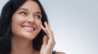 Sağlıklı ve parlak bir gülüşü olan genç bir kadın beyaz bir arka plana dikkatlice bakıyor. Güzellik, cilt bakımı, sağlık, ya da yaşam tarzı terfileri için harika, doğal ışıltıyı vurguluyor..