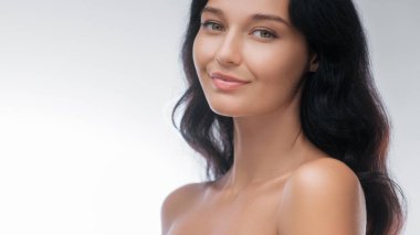 Uzun siyah saçlı, gülümseyen Asyalı bir kadın cilt bakımı stüdyosunda zarifçe poz veriyor ve kusursuz cildini ön plana çıkarıyor. Güzellik, cilt bakımı ve kozmetik reklamları için ideal, doğal zarafeti vurguluyor.