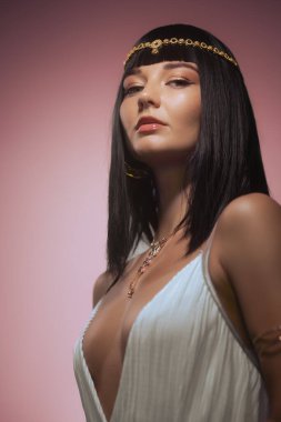 Uzun siyah saçlı, altın başlıklı beyaz bir elbise ve zarif bir kolye takan kendine güvenen bir kadın. Kleopatra 'dan esinlenilmiş bu görüntü güzellik, moda ve lüks kavramlar için mükemmeldir..