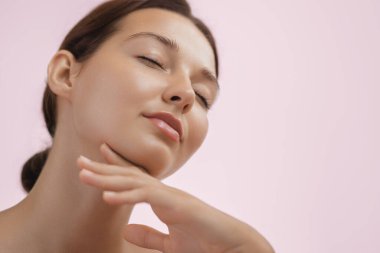 Kusursuz, pırıl pırıl cildi olan dingin genç bir kadın yüzünü ve boynunu nazikçe okşuyor, sakinlik ve rahatlama yayıyor. Cilt bakımını, sağlığı, güzelliği ve kendine bakımı teşvik etmek için mükemmel.